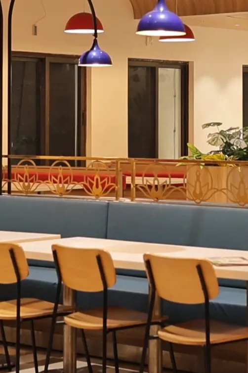 Modern vegetarian restaurant seating area at Annakoot Vrindavan with blue sofas, wooden chairs, hanging lamps, and clean sattvik dining ambience